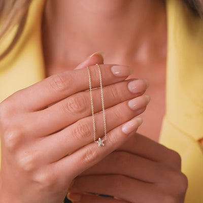 Dainty 14K yellow gold diamond star necklace held in a woman's hand with neutral nail polish.