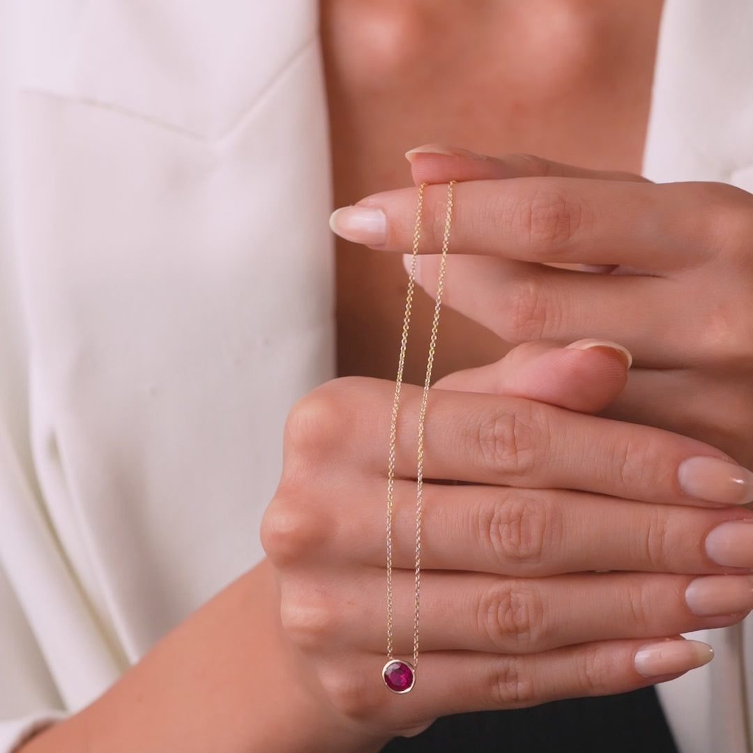 Model showcasing a 14K yellow gold 6mm bezel set ruby solitaire necklace, highlighting its minimalist design.