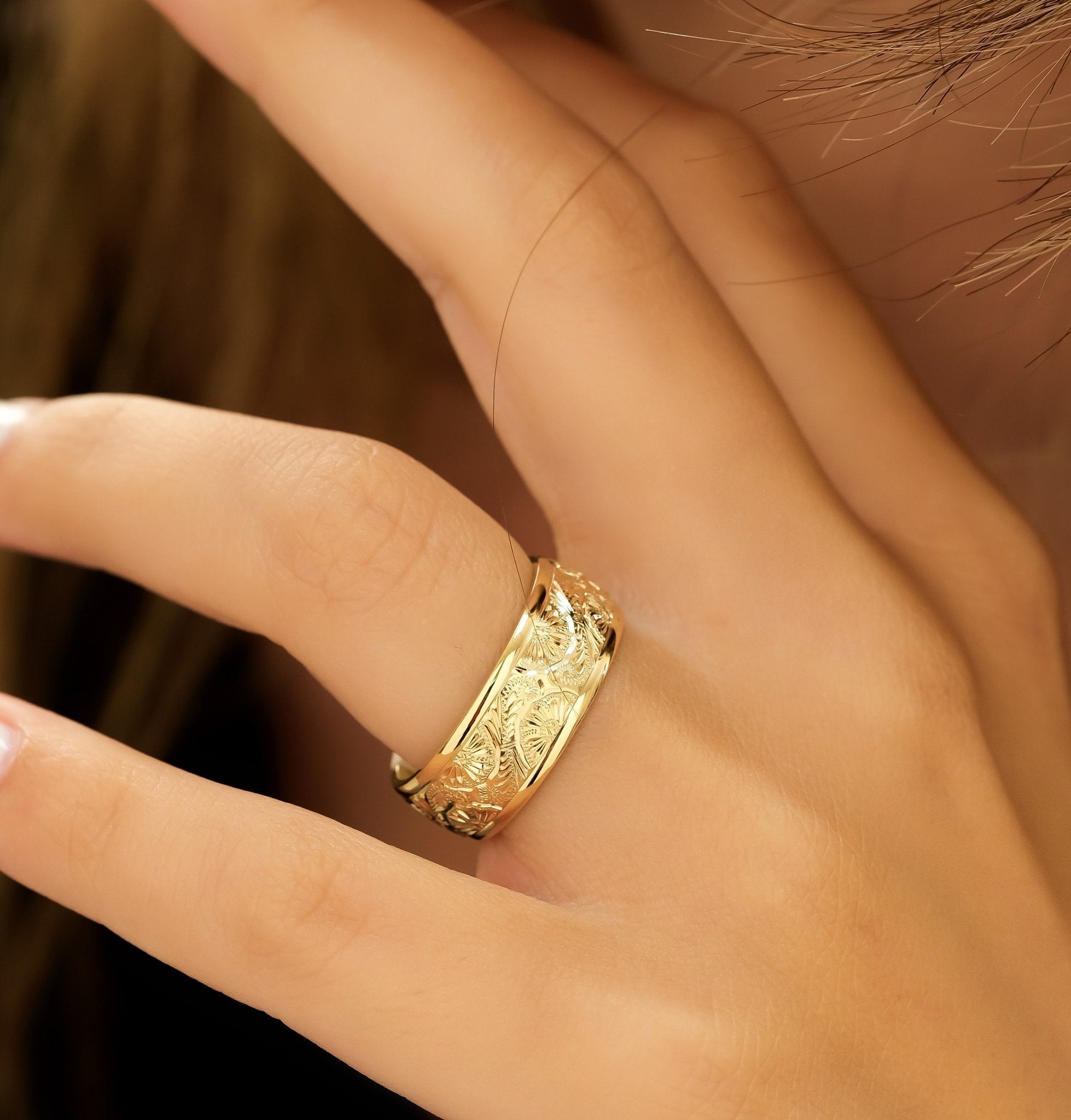 Hand engraved 8mm 14K yellow gold men's wedding band showcased on a finger, featuring a shiny leaf motif.