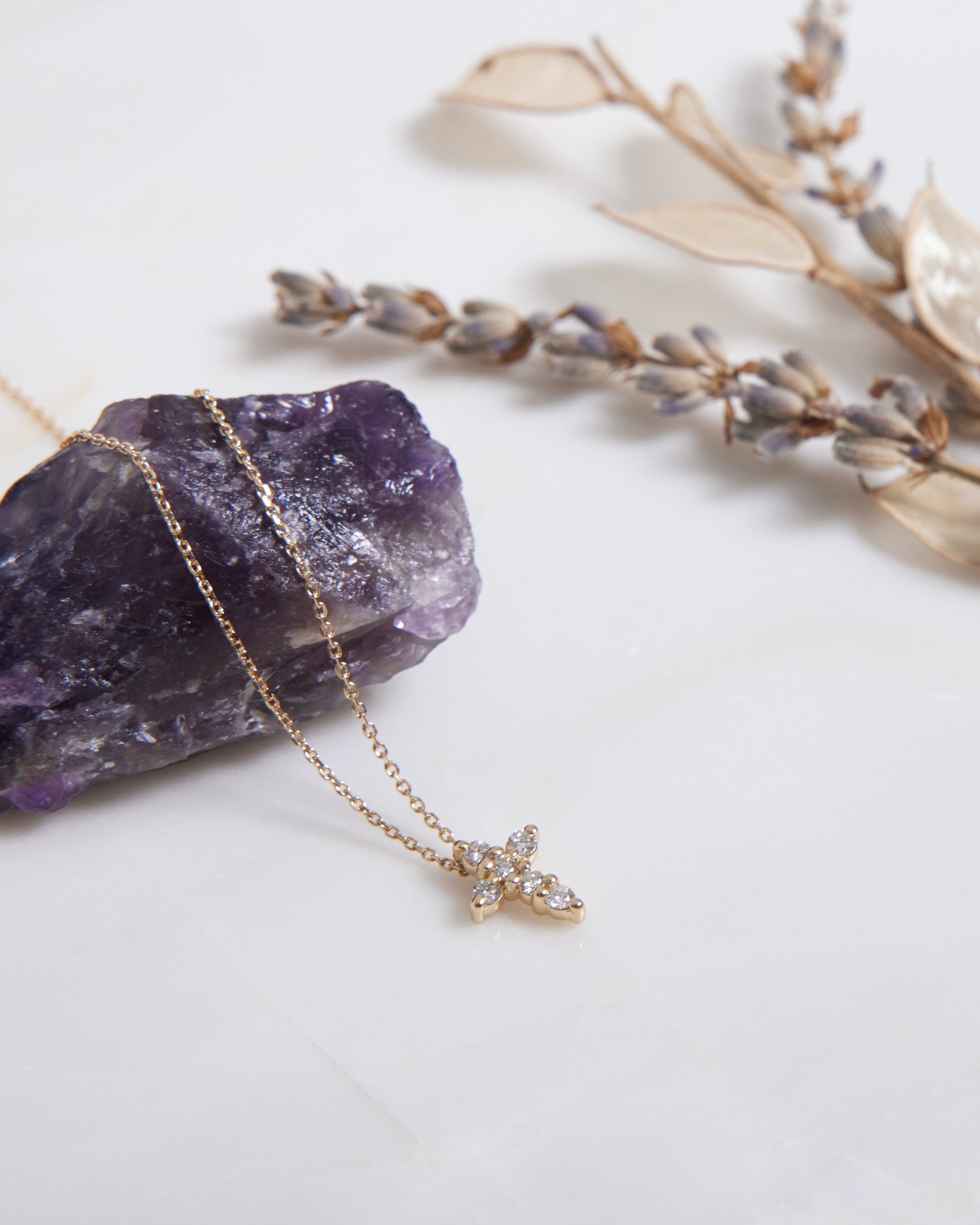14K solid white gold minimalist diamond cross necklace resting on amethyst crystal with dried flowers.