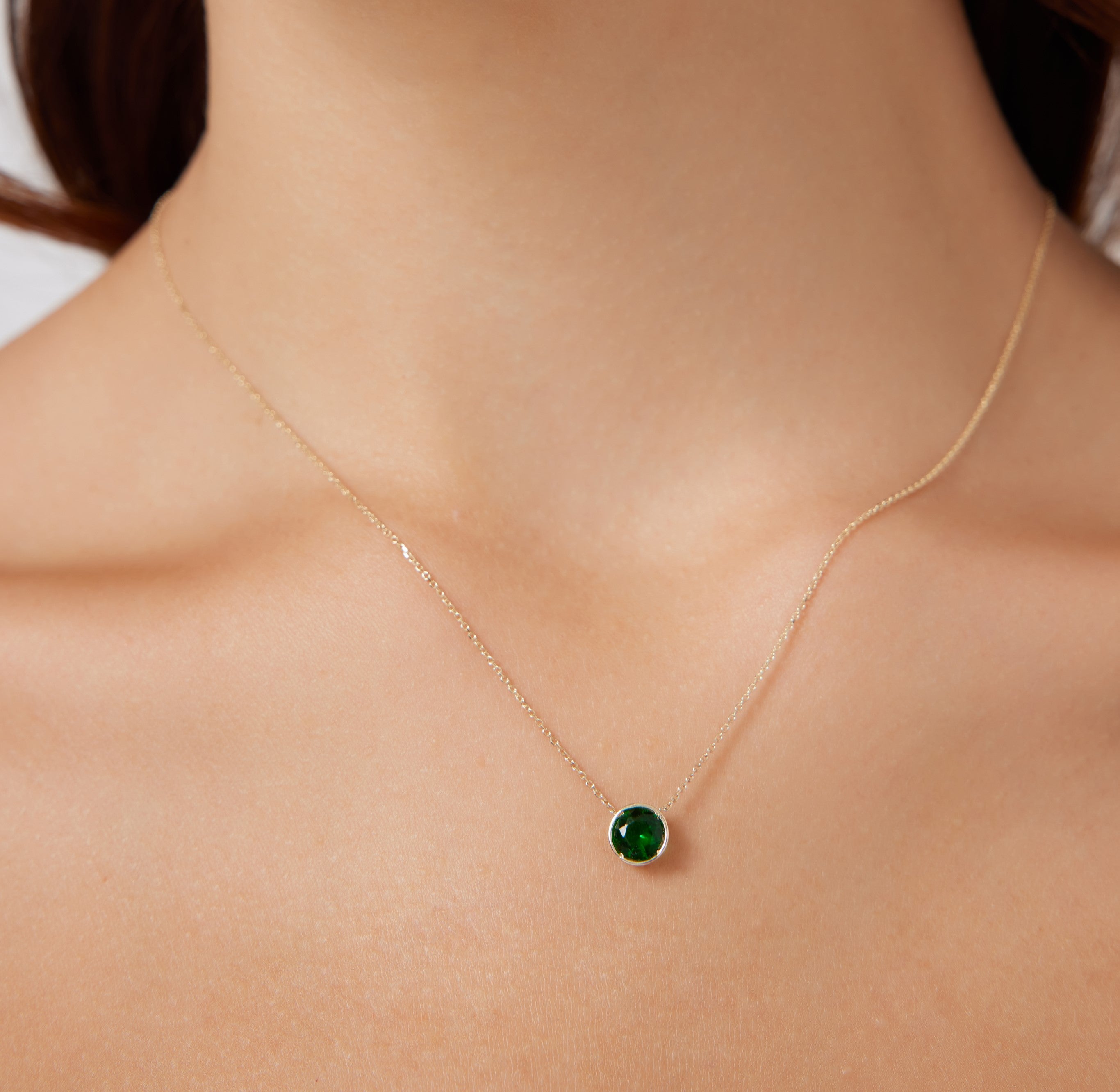 14K yellow gold 6mm bezel set emerald solitaire necklace worn on a model's neck, perfect for everyday elegance.