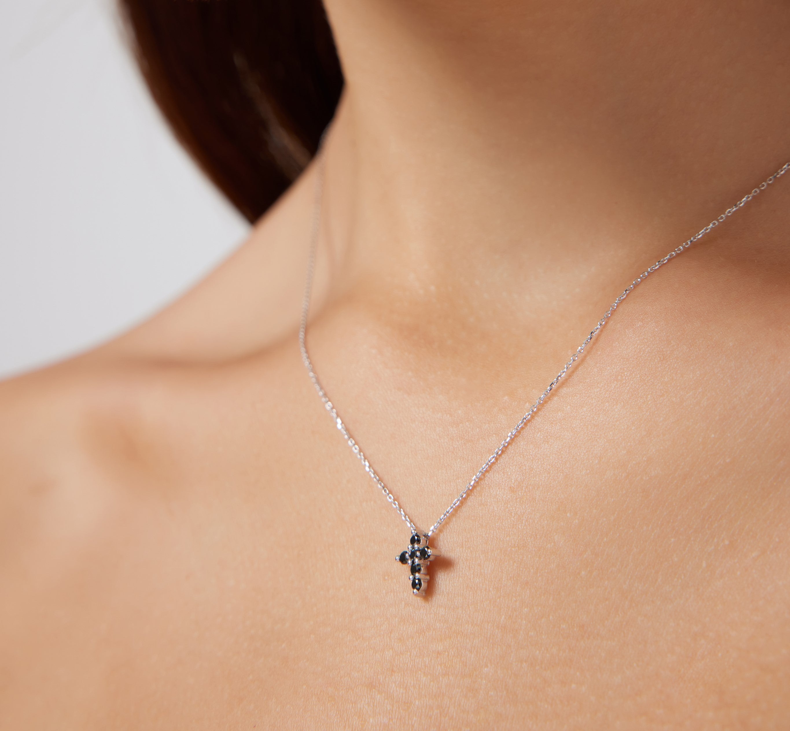 Minimalist 14K solid white gold cross necklace featuring black diamonds, worn elegantly on the neck.