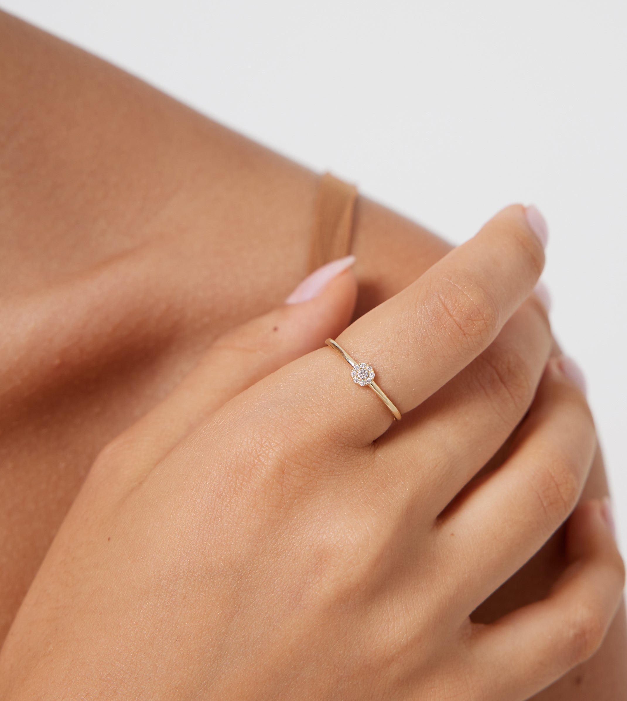 Minimalist 14K gold halo diamond ring worn on a woman's hand, showcasing its dainty design and shiny finish.
