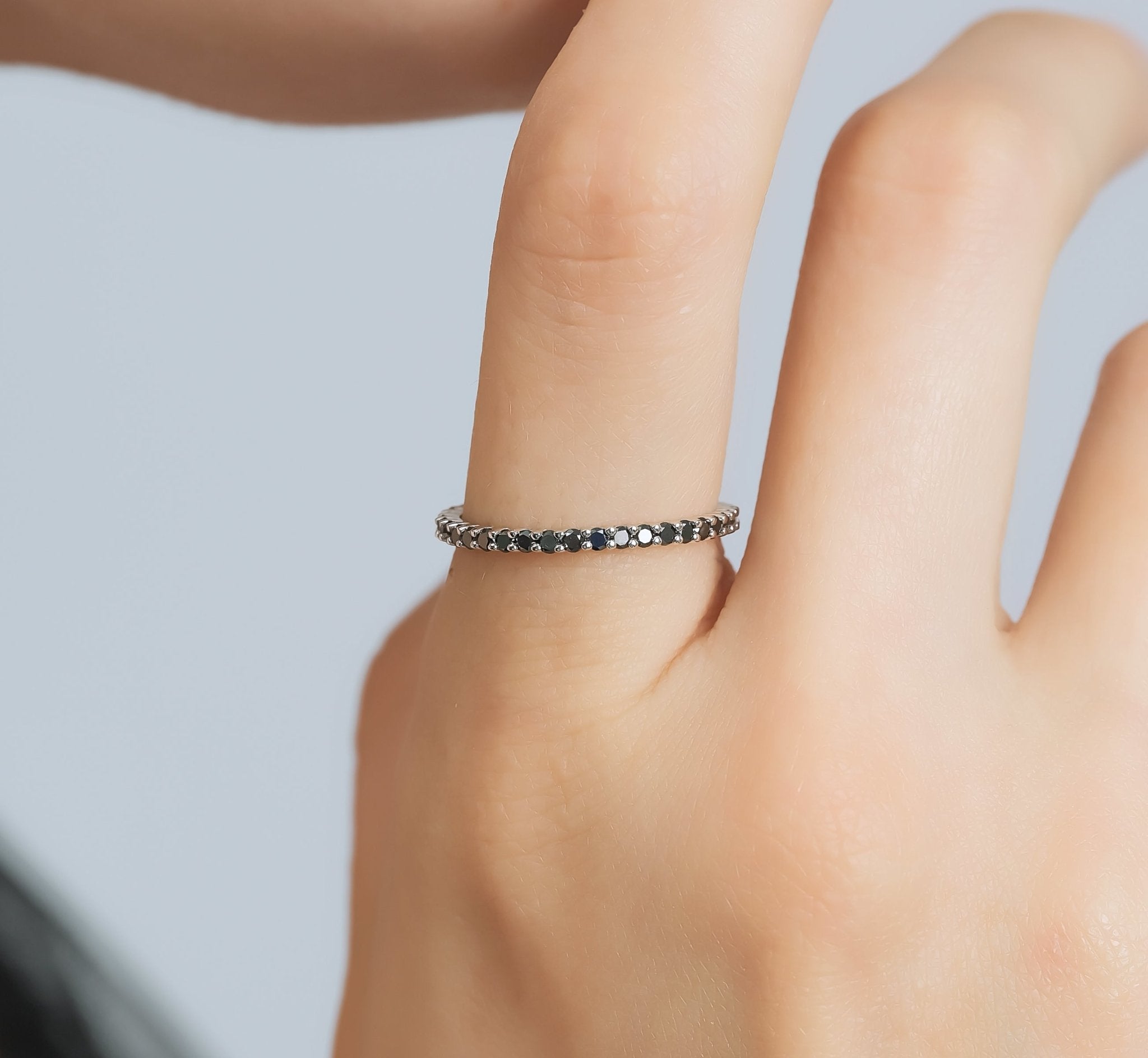14K gold black diamond full eternity wedding ring on a finger, showcasing prong setting with elegant black diamonds.
