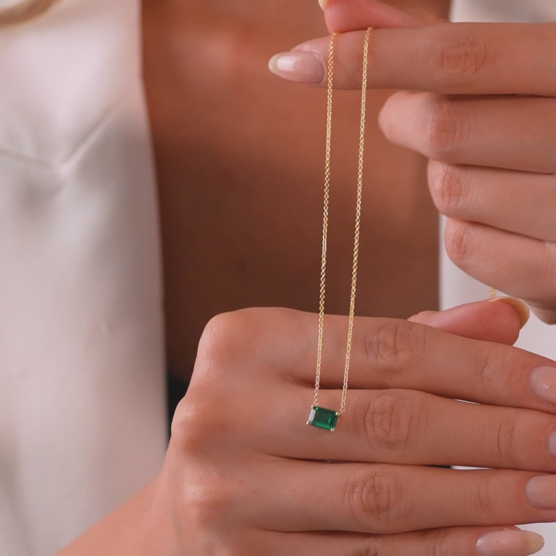Model holding a 14K white gold emerald cut solitaire emerald necklace, featuring a delicate design.