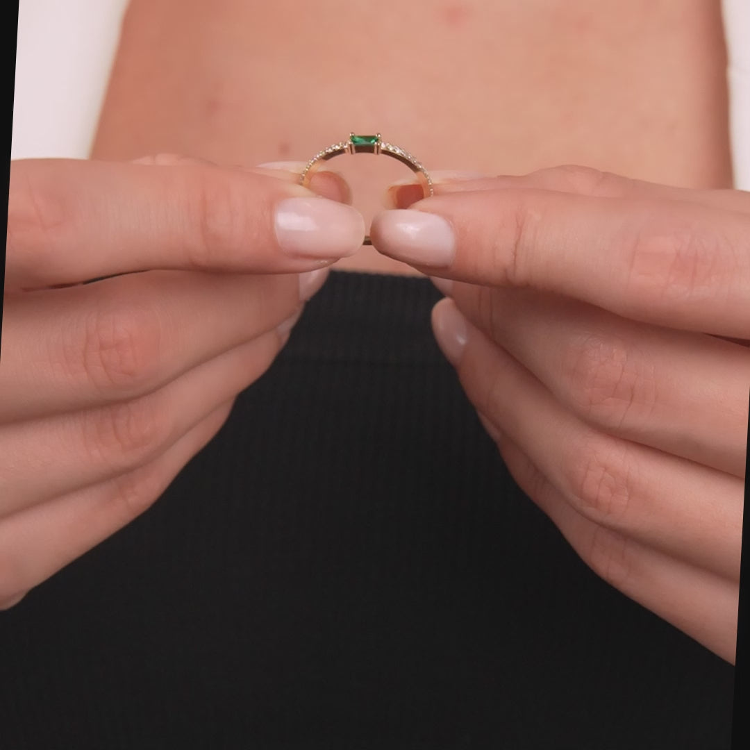 Woman's hands holding a 14K yellow gold minimalist wedding ring with an emerald and diamond accent.
