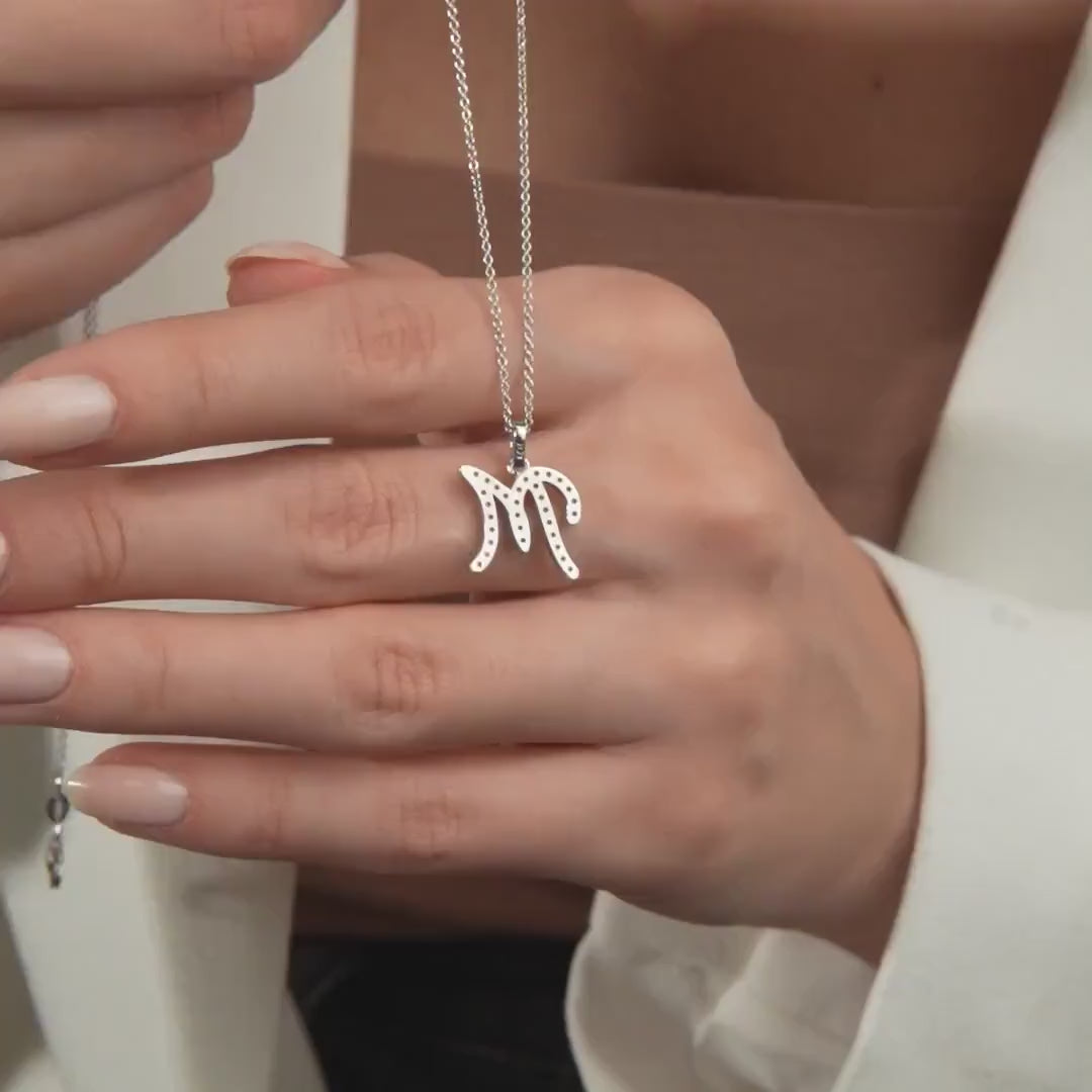 14K white gold initial necklace featuring a script letter M, showcased on a hand with a neutral background.