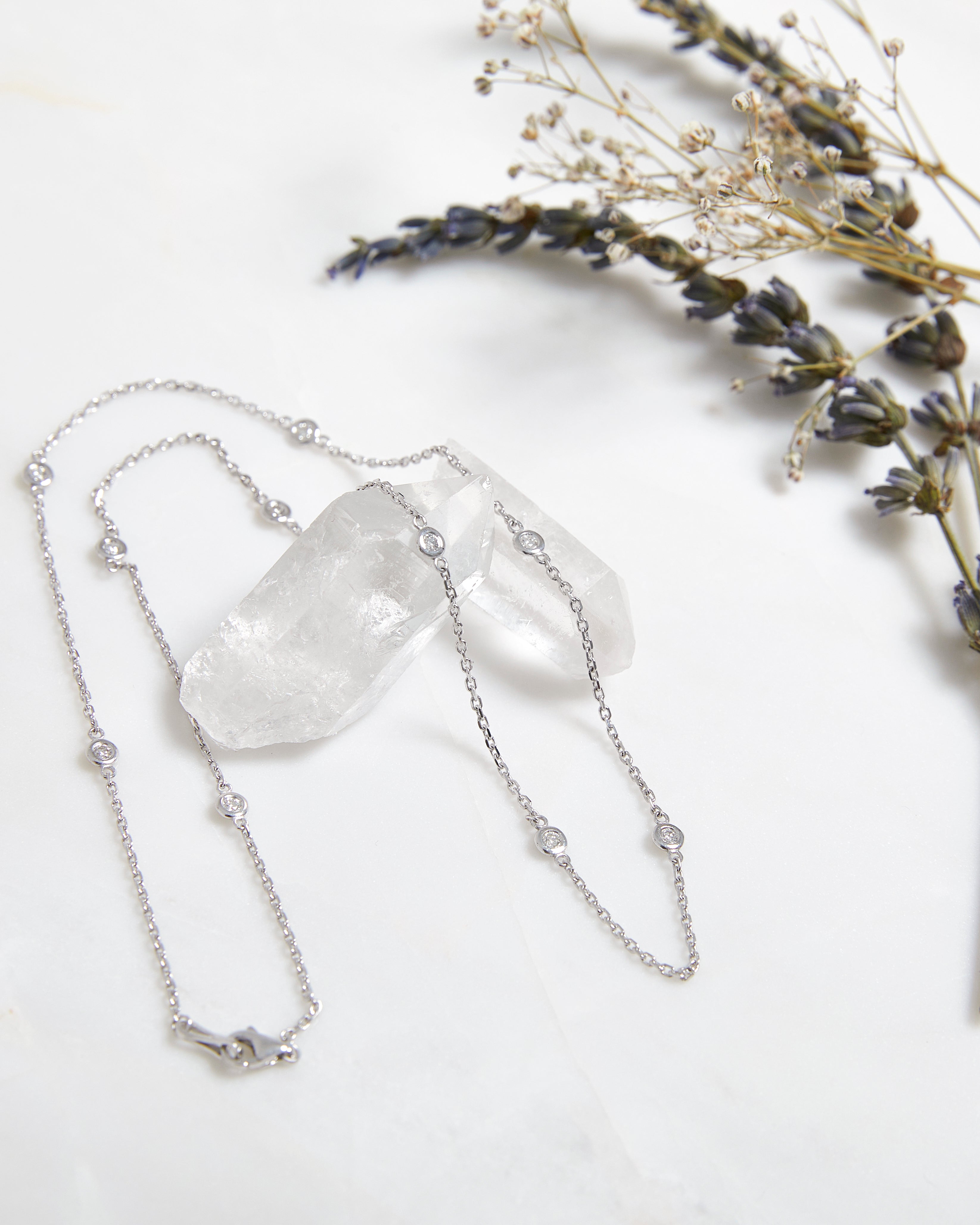 14K gold diamond station necklace on a marble surface with lavender and quartz crystals, displaying delicate diamond stations.