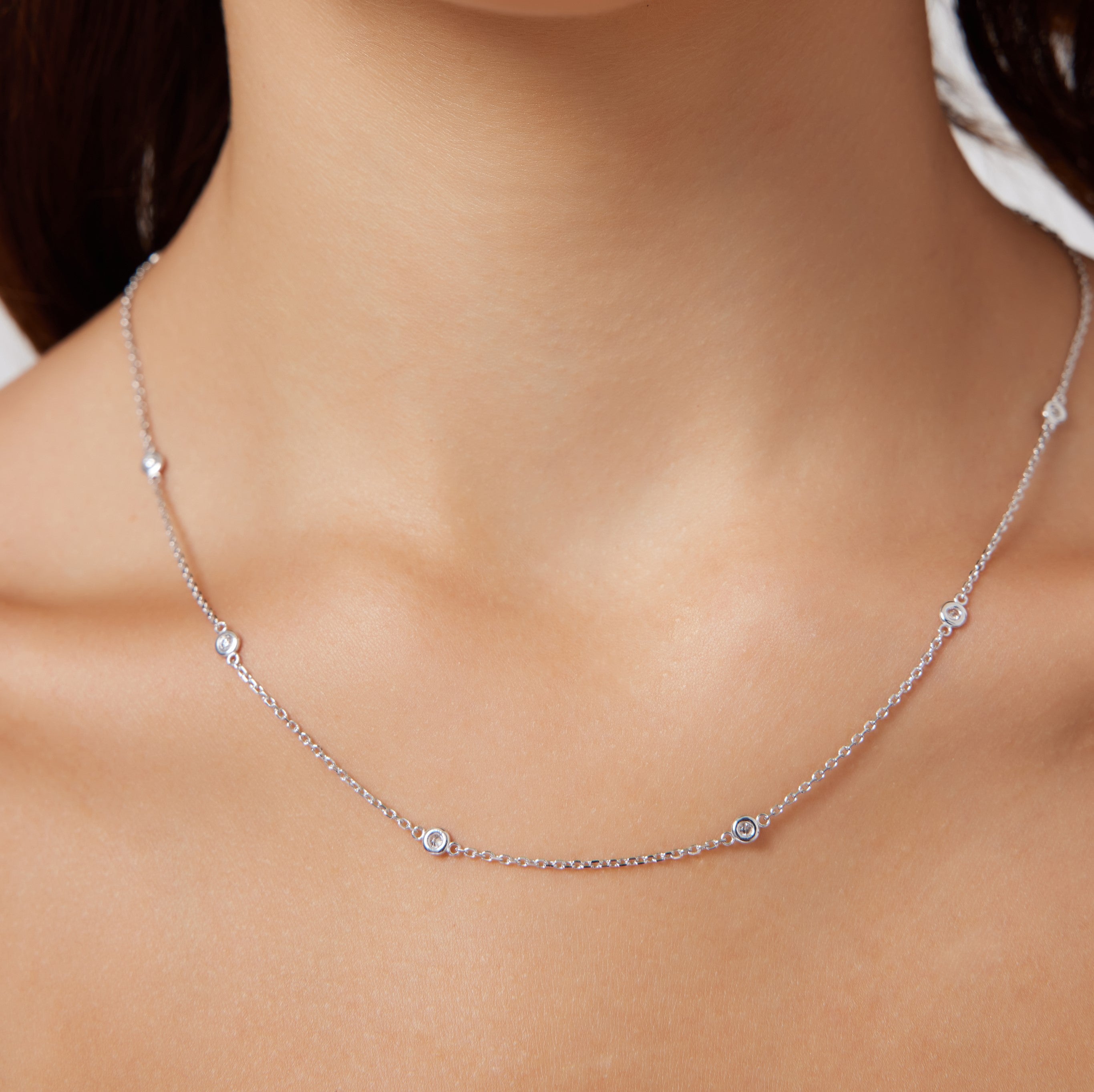 Dainty 14K gold diamond station necklace displayed on a model's neckline, featuring bezel set diamonds.