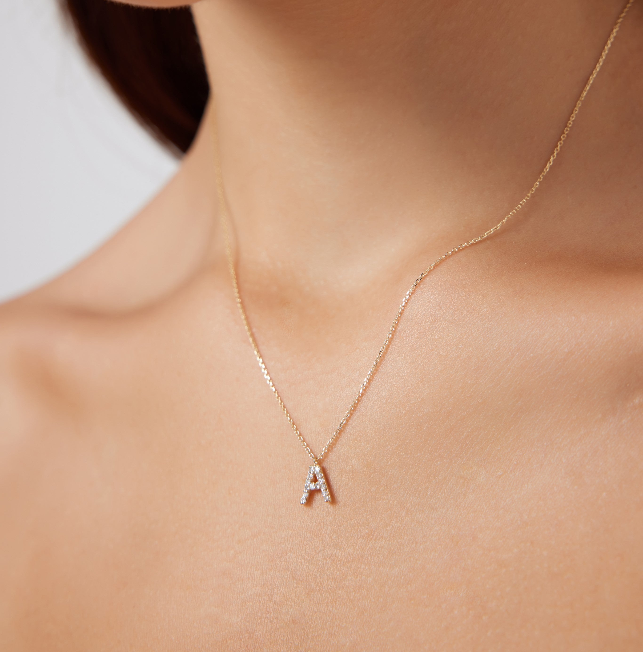 14K yellow gold diamond initial necklace featuring letter A, delicately worn on a woman's neck.