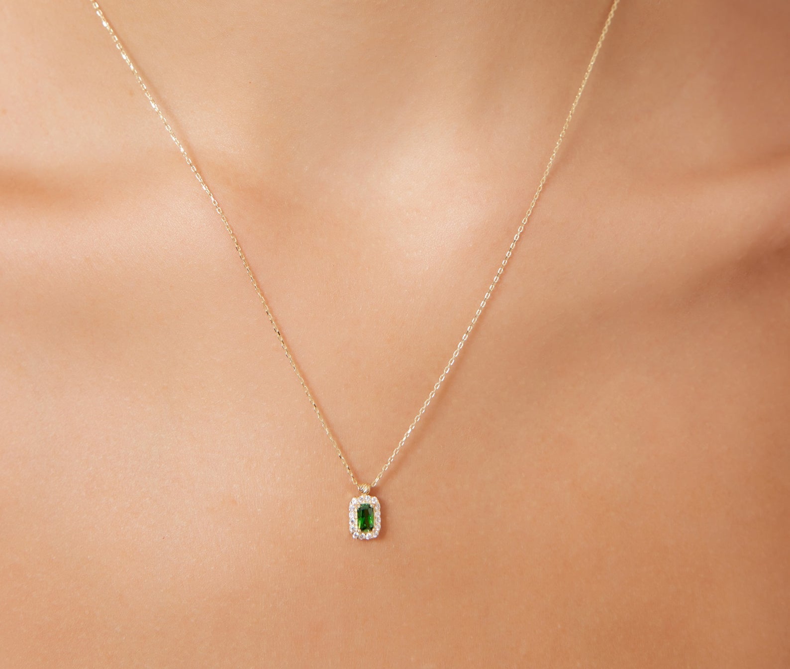 14K yellow gold emerald cut solitaire emerald necklace worn on a model's neck, showcasing its elegant design and sparkle.