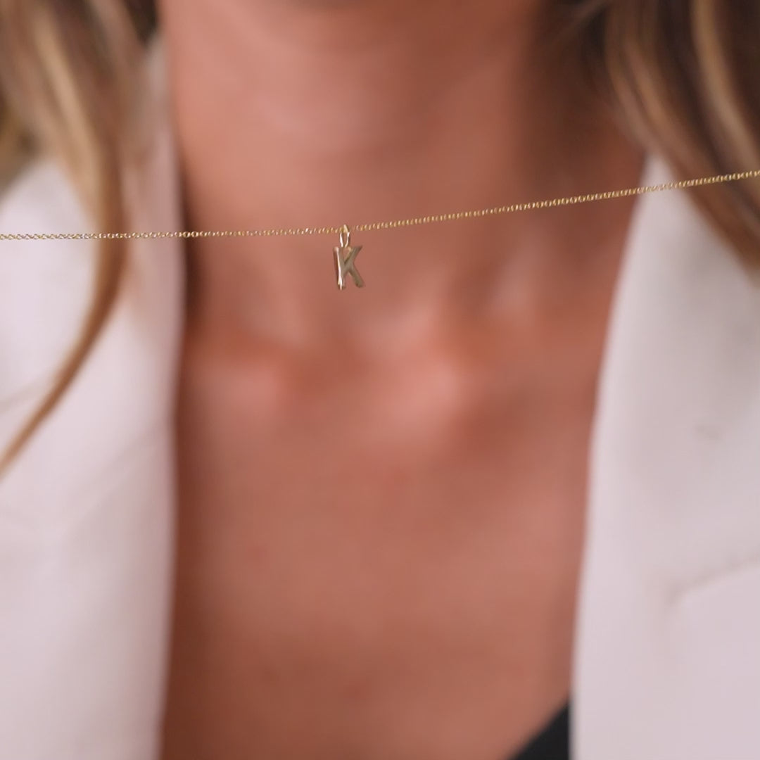 14K solid yellow gold initial necklace featuring the letter K, elegantly displayed on a woman.