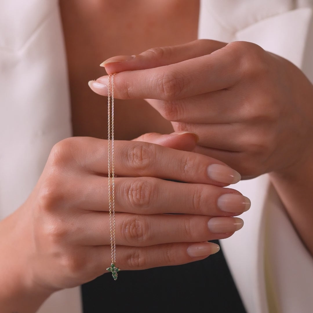 Model showcasing a delicate 14K solid yellow gold emerald cross necklace held in hands.