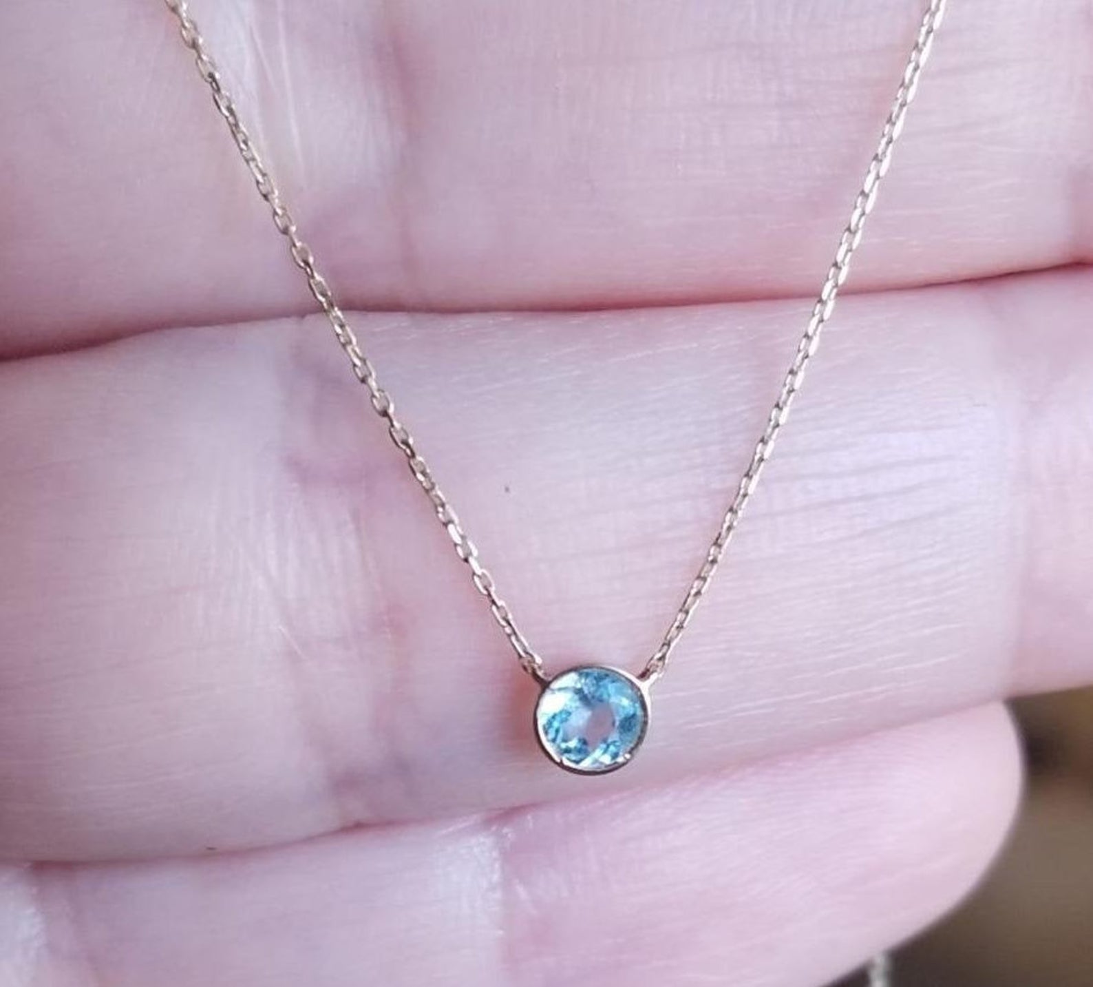 14K yellow gold 4mm bezel set aquamarine solitaire necklace held in hand, minimalist design for everyday wear.