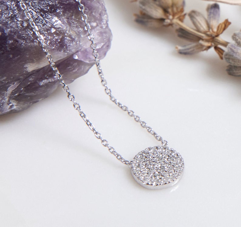14K white gold diamond circle necklace resting on a stone, featuring a sparkling diamond disk pendant.