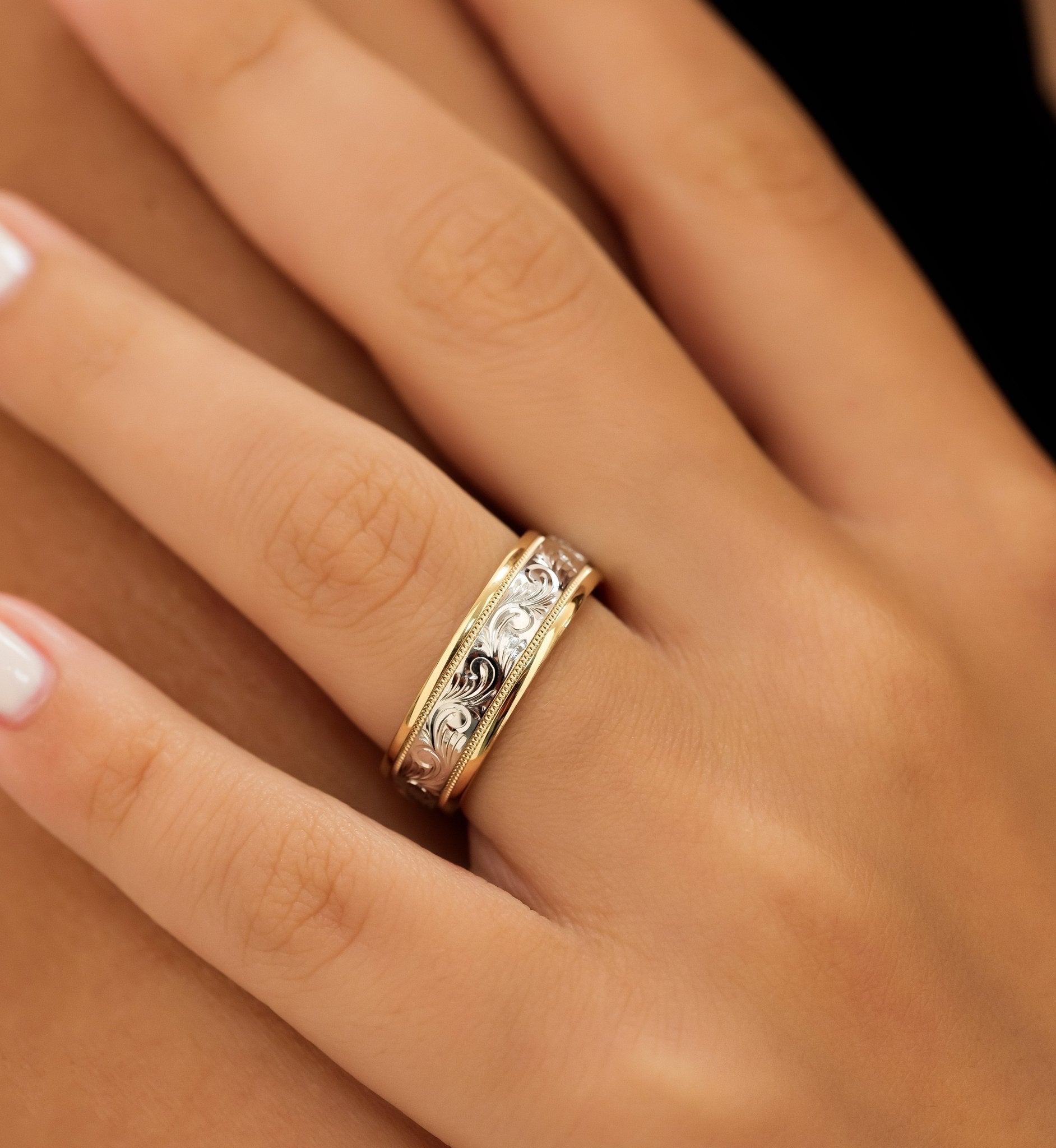 Two tone gold hand engraved men's wedding band on a finger, showcasing its shiny finish and intricate design.
